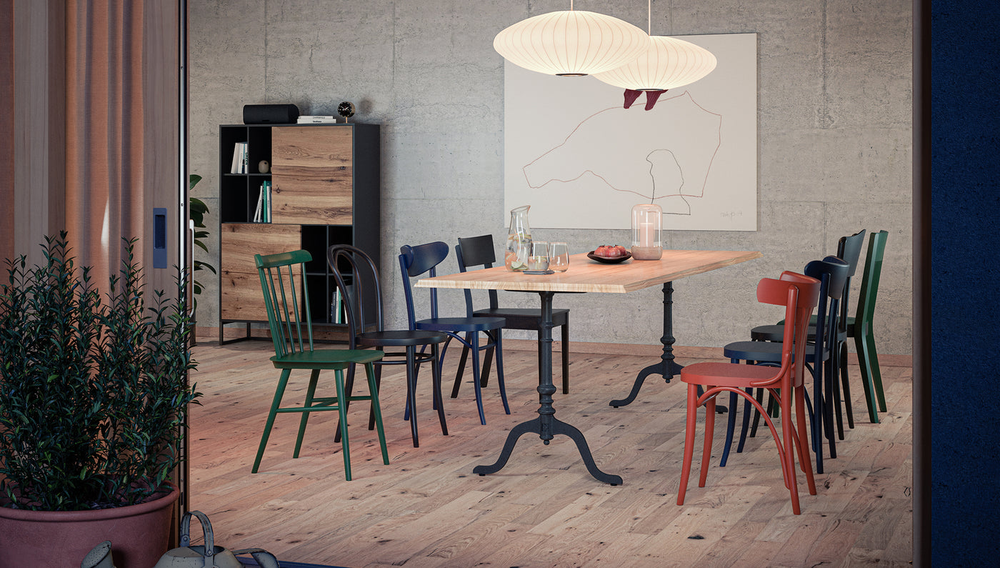 Großer Beizentisch aus Massivholz mit schwarzen Gusseisenfüssen umgeben von bunten Holzstühlen in modernem Esszimmer Ambiente