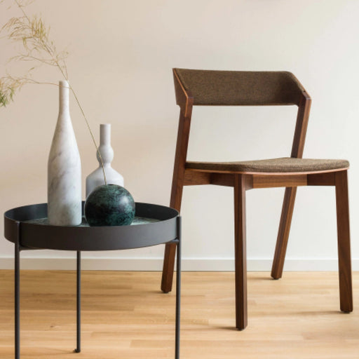 Moderner Esszimmerstuhl aus dunklem Massivholz mit braunem Polstersitz und kantigem Design im Vordergrund vor heller Wand