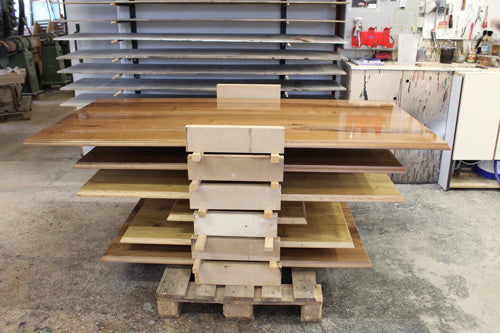 Gestapelte Tischplatten aus Massivholz in einer Schreinerei während der Produktion. Die Platten werden sorgfältig verarbeitet und vorbereitet, um stabile Beizentische, Restauranttische und individuelle Maßanfertigungen zu fertigen.