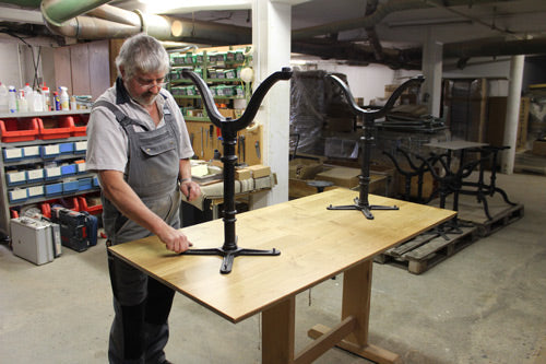 Handwerker montiert schwarzen Gussfuß an Holztischplatte in Werkstatt traditionelle Schweizer Fertigung für robuste Beizentische